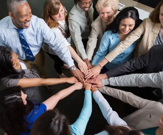 Diverse group of smiling businesspeople joining hands together in the center of a circle, symbolizing teamwork and collaboration in the workplace